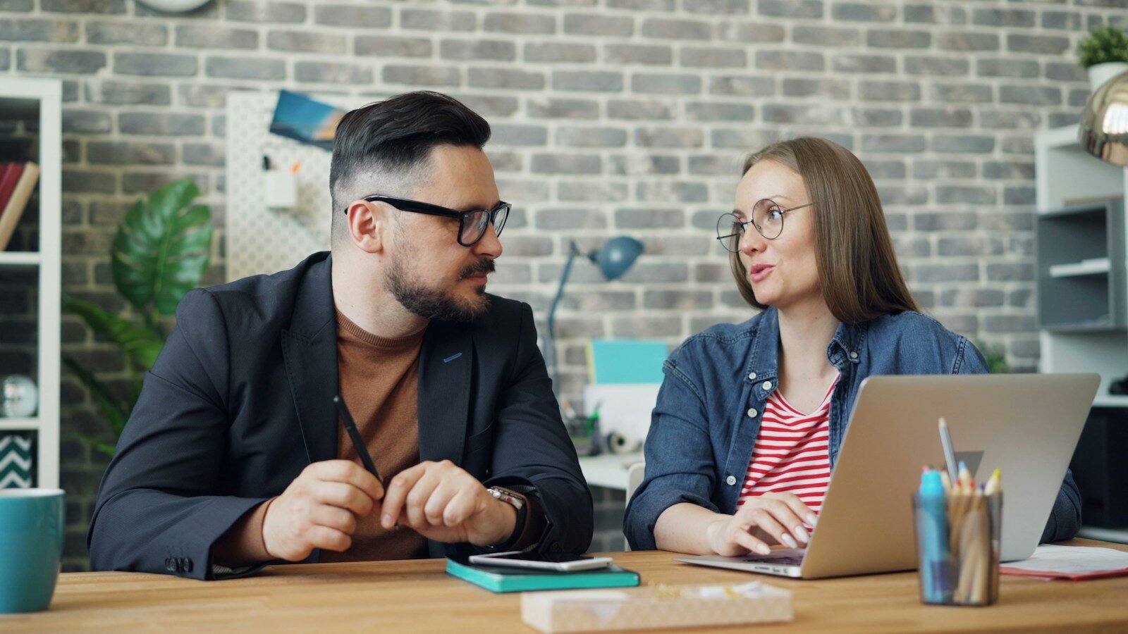 Photo by Vitaly Gariev a man and a woman sitting at a table looking at a laptop